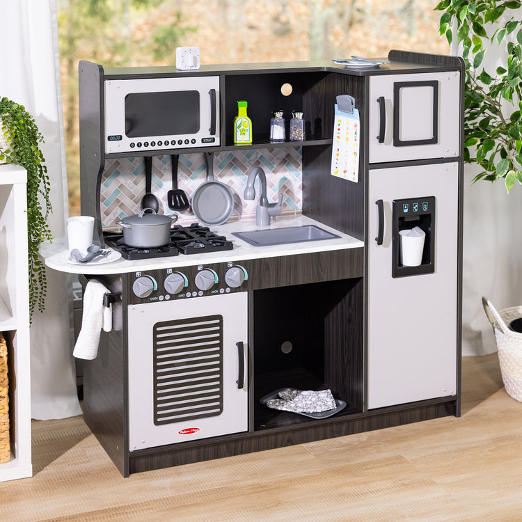 A playroom scene with The Melissa & Doug Chef's Wooden Pretend Play Kitchen for Kids With “Ice” Cube Dispenser – Charcoal Gray