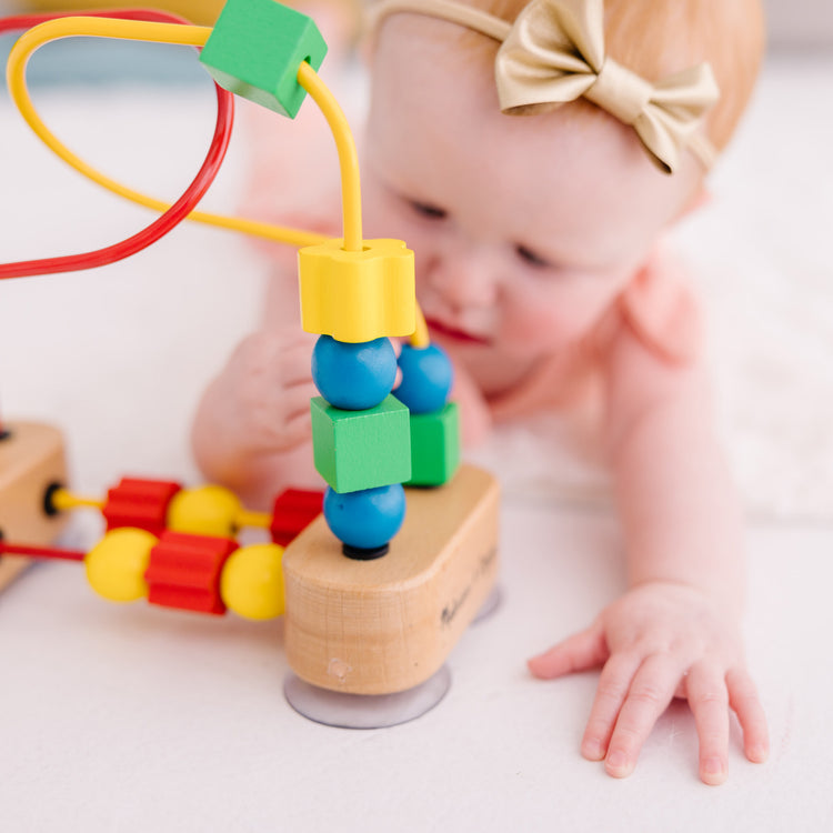 A kid playing with The Melissa & Doug First Bead Maze - Wooden Educational Toy for Floor, High Chair, or Table