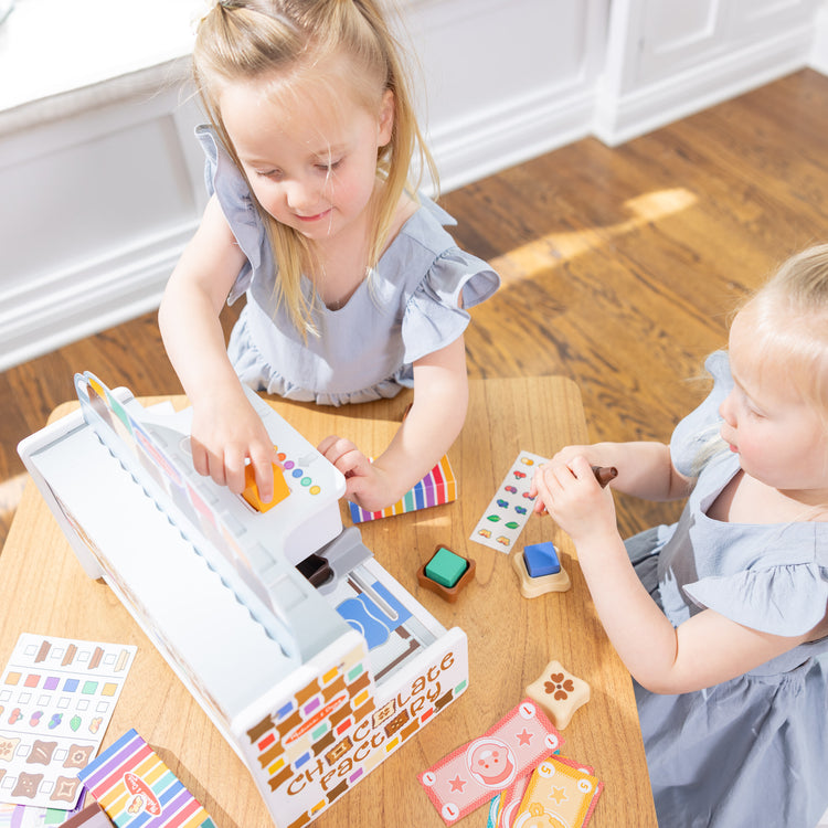 A kid playing with The Melissa & Doug Wooden Chocolate Factory Pretend Play Set, Play Food Candy Maker for Boys and Girls