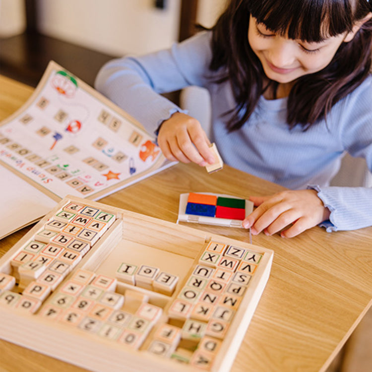 A kid playing with The Melissa & Doug Deluxe Letters and Numbers Wooden Stamp Set ABCs 123s With Activity Book, 4-Color Stamp Pad