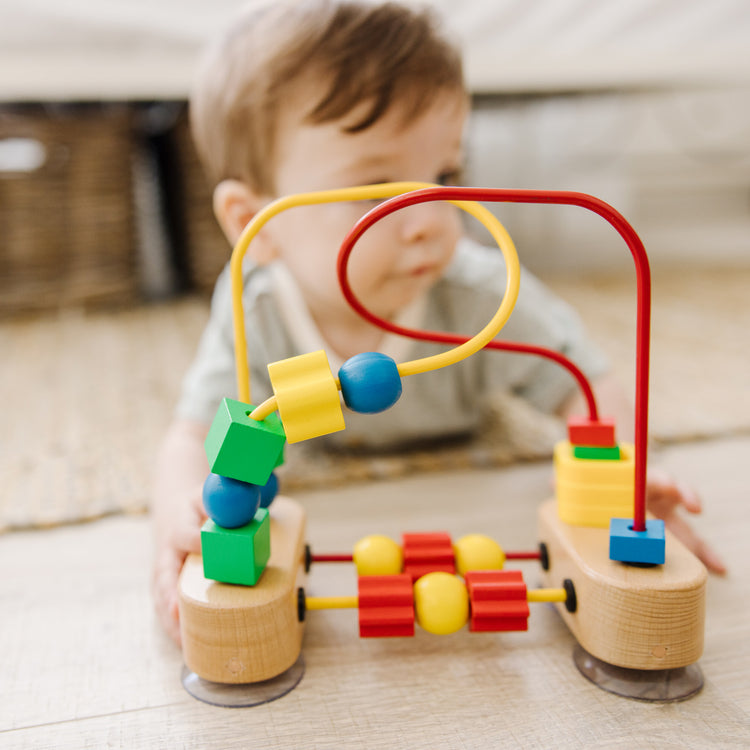 A kid playing with The Melissa & Doug First Bead Maze - Wooden Educational Toy for Floor, High Chair, or Table