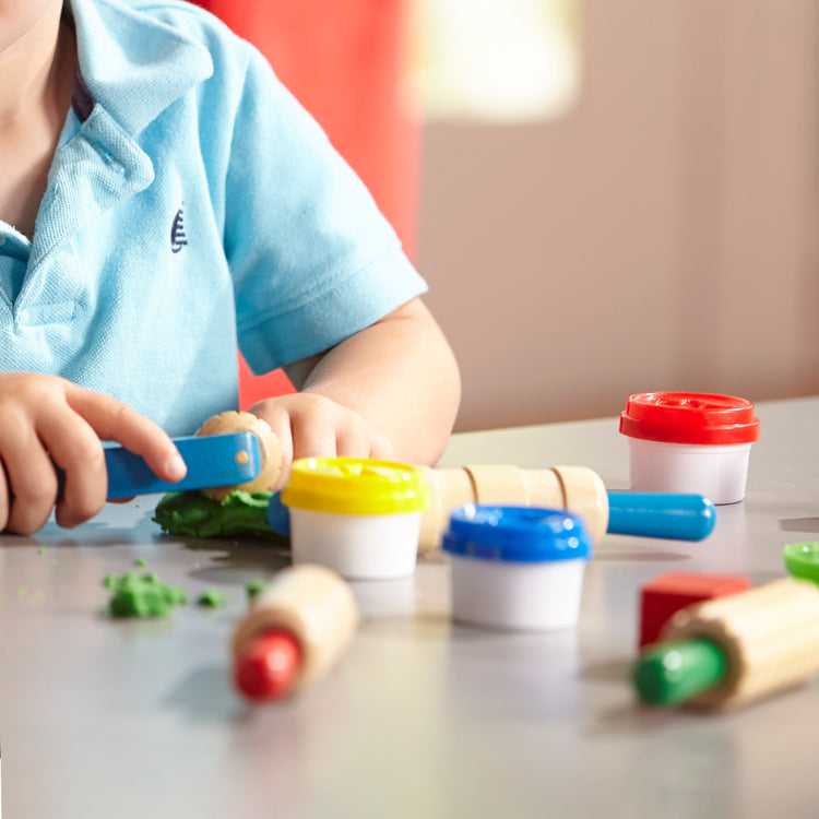 A kid playing with The Melissa & Doug Shape, Model, and Mold Craft Activity Set - 4 Tubs of Modeling Dough and Tools