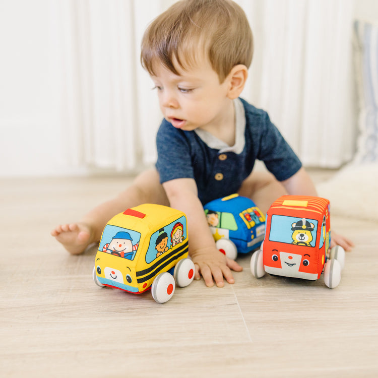 A kid playing with The Melissa & Doug K's Kids Pull-Back Vehicle Set - Soft Baby Toy Set With 4 Cars and Trucks 