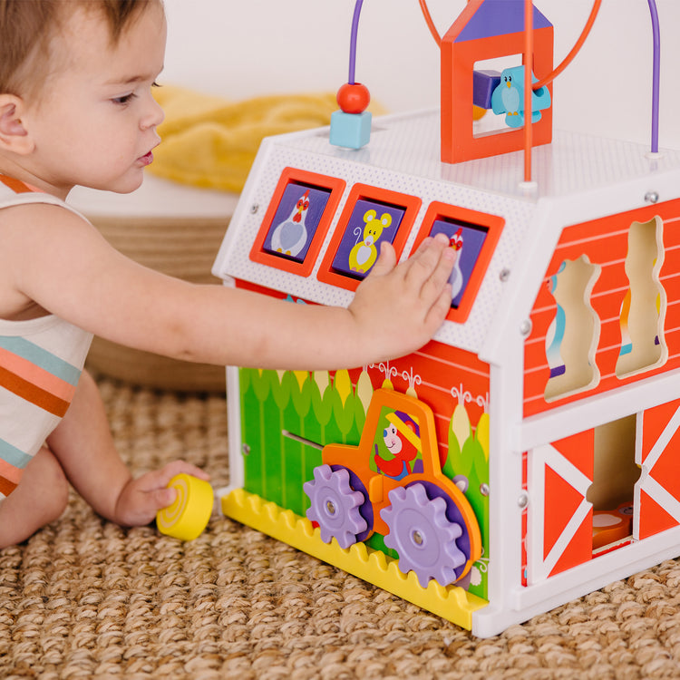 A kid playing with The Melissa & Doug First Play Slide, Sort & Roll Wooden Activity Barn with Bead Maze, 6 Wooden Play Pieces (11.75” x 11.75” x 20” Assembled)