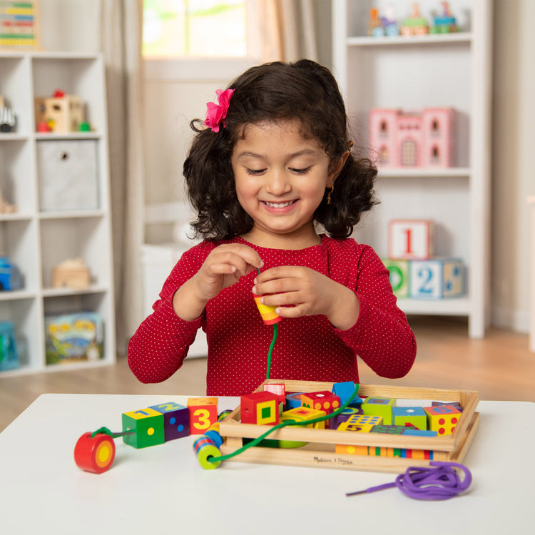 A kid playing with The Melissa & Doug Deluxe Wooden Lacing Beads - Educational Activity With 27 Beads and 2 Laces