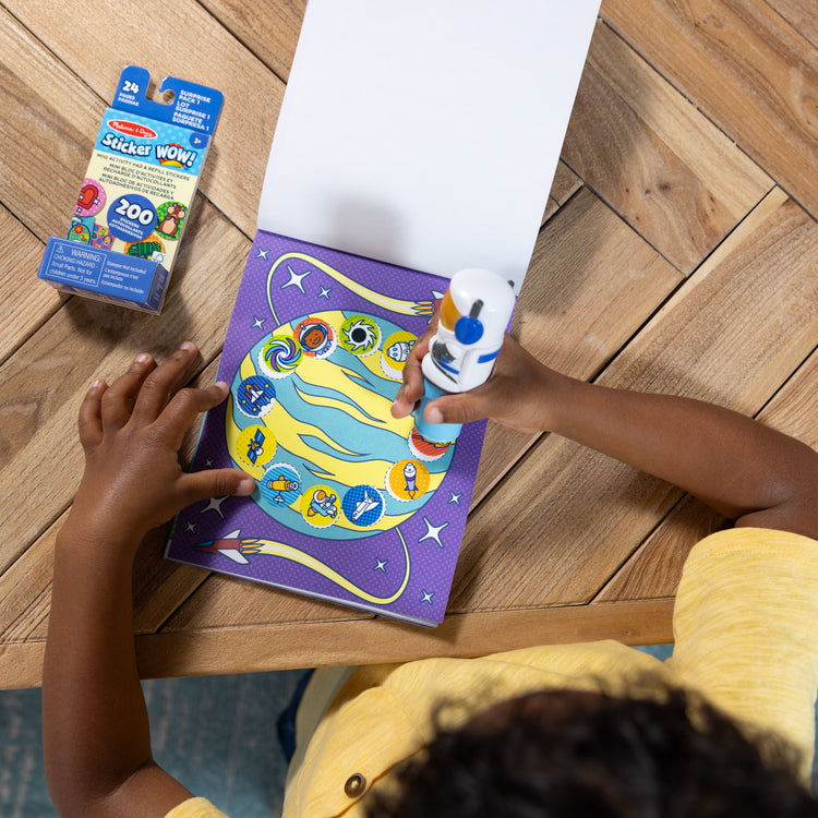 A kid playing with The Melissa & Doug Sticker WOW!™ Astronaut Bundle: 24-Page Activity Pad, Sticker Stamper, Mini Activity Pad, 500 Stickers, Arts and Crafts Fidget Toy Collectible Character