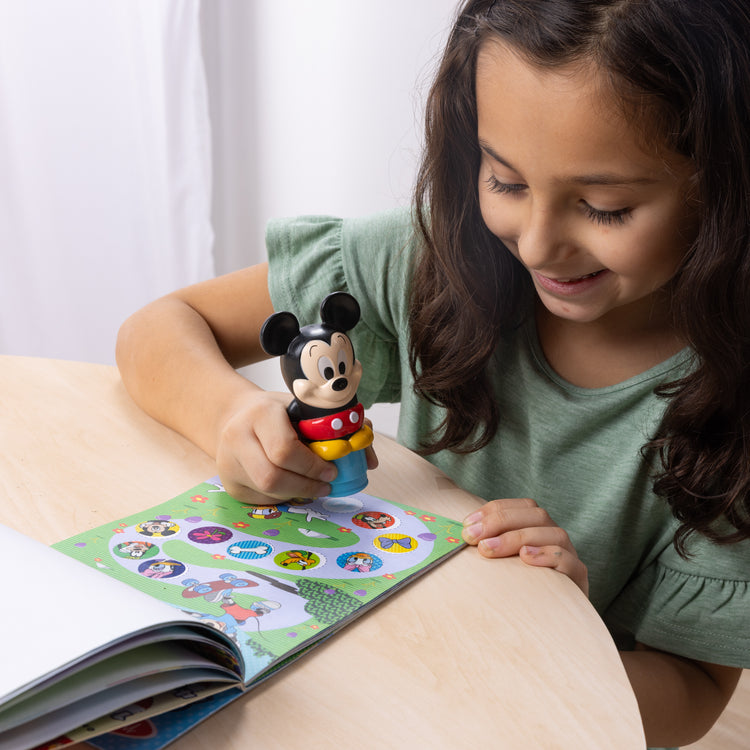 A kid playing with The Melissa & Doug Sticker WOW!™ 24-Page Activity Pad and Sticker Stamper, 300 Stickers, Arts and Crafts Fidget Toy Collectible Character – Disney Mickey Mouse

