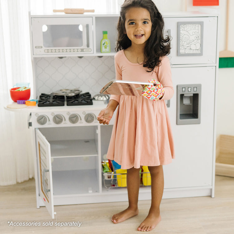 A kid playing with The Melissa & Doug Wooden Chef’s Pretend Play Toy Kitchen With “Ice” Cube Dispenser – Cloud White