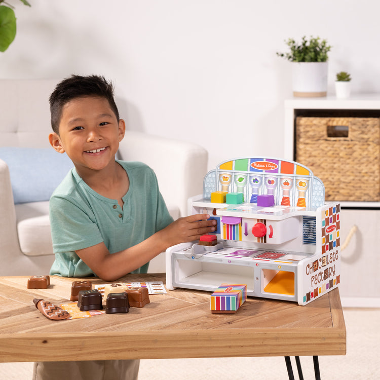 A kid playing with The Melissa & Doug Wooden Chocolate Factory Pretend Play Set, Play Food Candy Maker for Boys and Girls