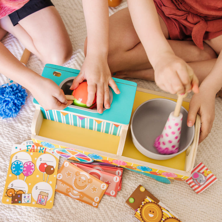 A kid playing with The Melissa & Doug Fun at the Fair! Wooden Carnival Candy Tabletop Cart and Play Food Set