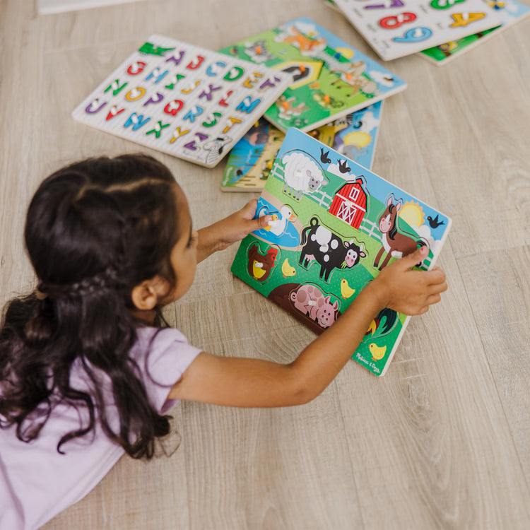 A kid playing with The Melissa & Doug Wooden Peg Puzzle 6-Pack – Numbers, Letters, 3 Animals, Vehicles