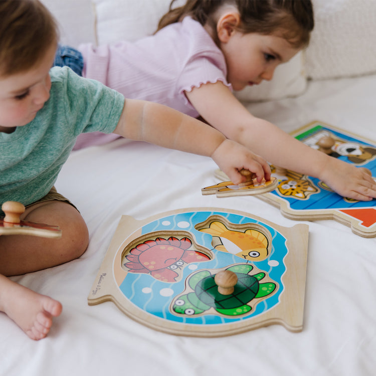 A kid playing with The Melissa & Doug Animals Jumbo Knob Wooden Puzzles Set - Fish and Pets