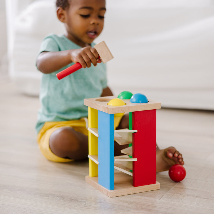 A kid playing with The Melissa & Doug Deluxe Pound and Roll Wooden Tower Toy With Hammer