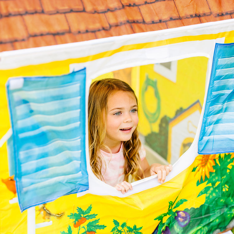 A kid playing with The Melissa & Doug Cozy Cottage Fabric Play Tent and Storage Tote