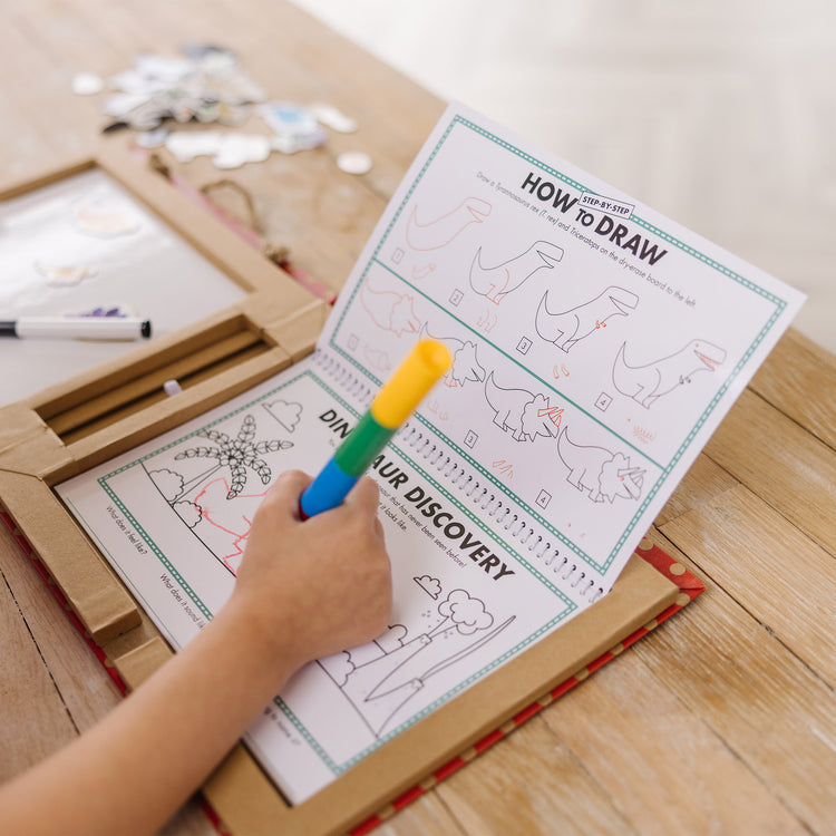 A kid playing with The Melissa & Doug Natural Play: Play, Draw, Create Dinosaurs Drawing Activity Set & Magnet Kit - Reusable Mess-Free Travel Activity