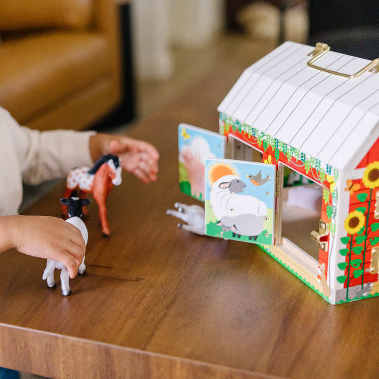 A kid playing with The Melissa & Doug Latches Wooden Activity Barn with 5 Doors, 4 Play Figure Farm Animals