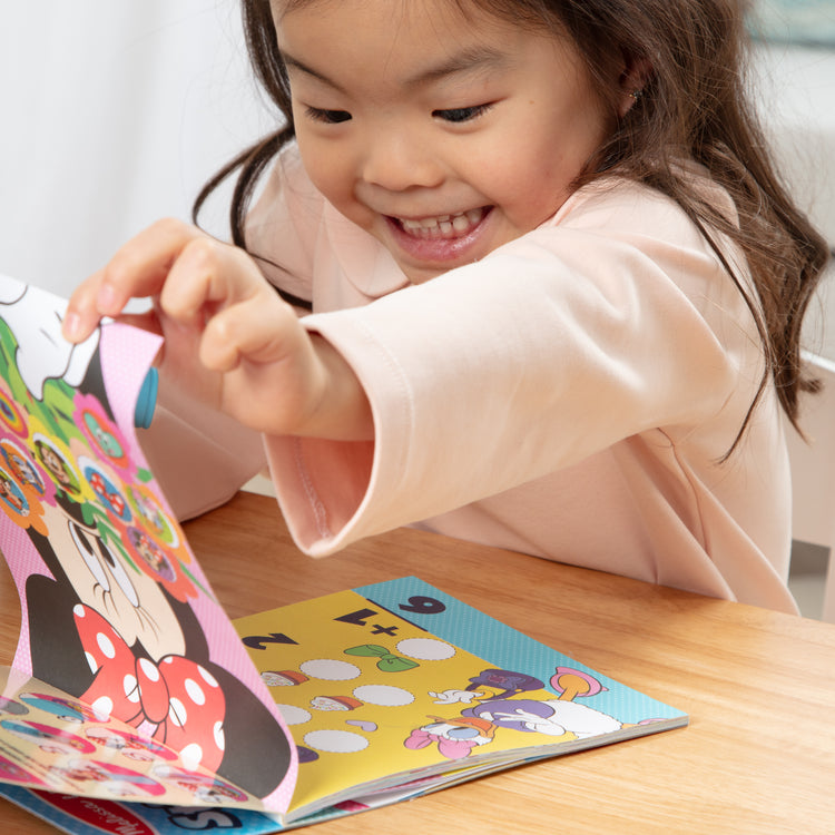 A kid playing with The Melissa & Doug Sticker WOW!™ 24-Page Activity Pad and Sticker Stamper, 300 Stickers, Arts and Crafts Fidget Toy Collectible Character – Disney Minnie Mouse