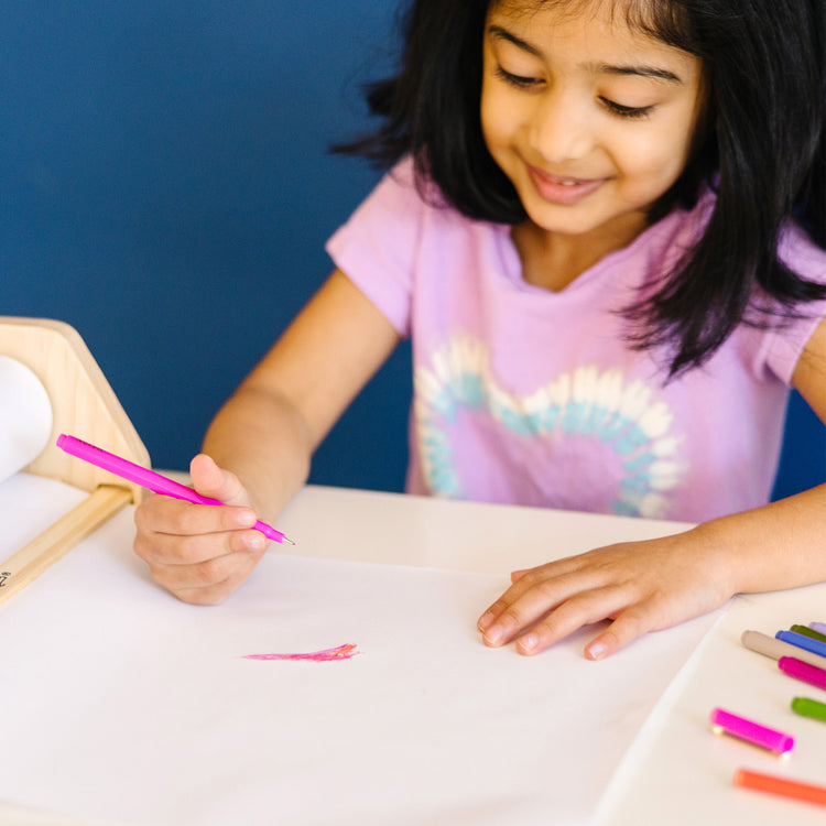 A kid playing with The Melissa & Doug Tabletop Easel Paper Roll (12 inches x 75 feet), 3-Pack