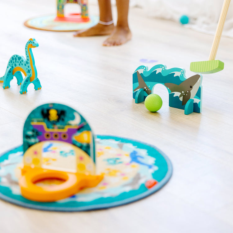 A kid playing with The Melissa & Doug Fun at the Fair! Mini Golf Play Set – 3 Multi-Themed Holes and Wooden Obstacles