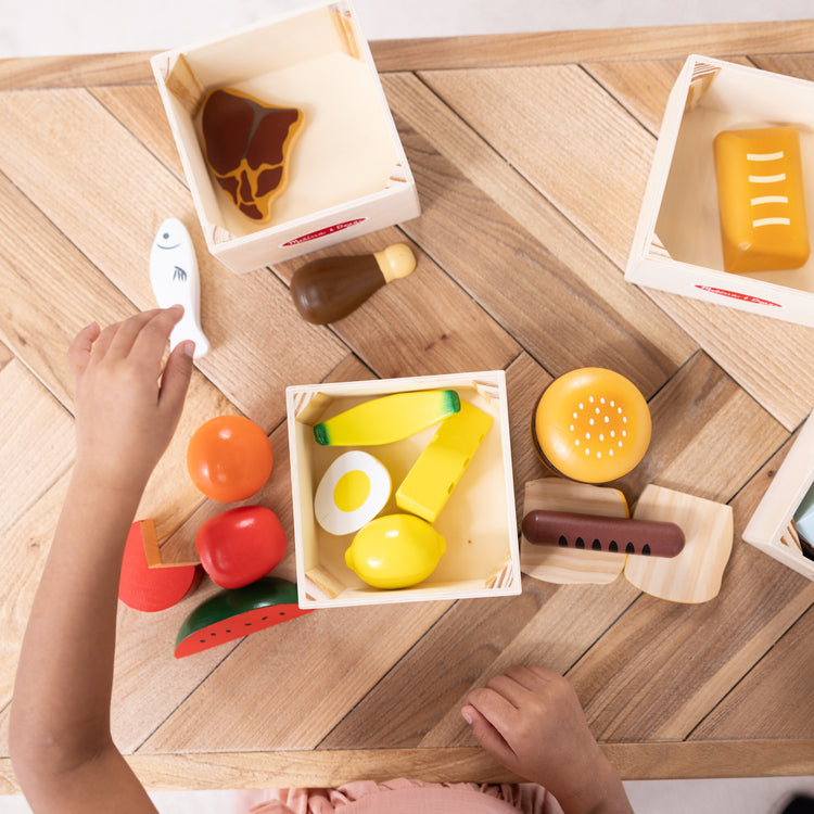 A kid playing with The Melissa & Doug Food Groups - 21 Wooden Pieces and 4 Crates, Multi