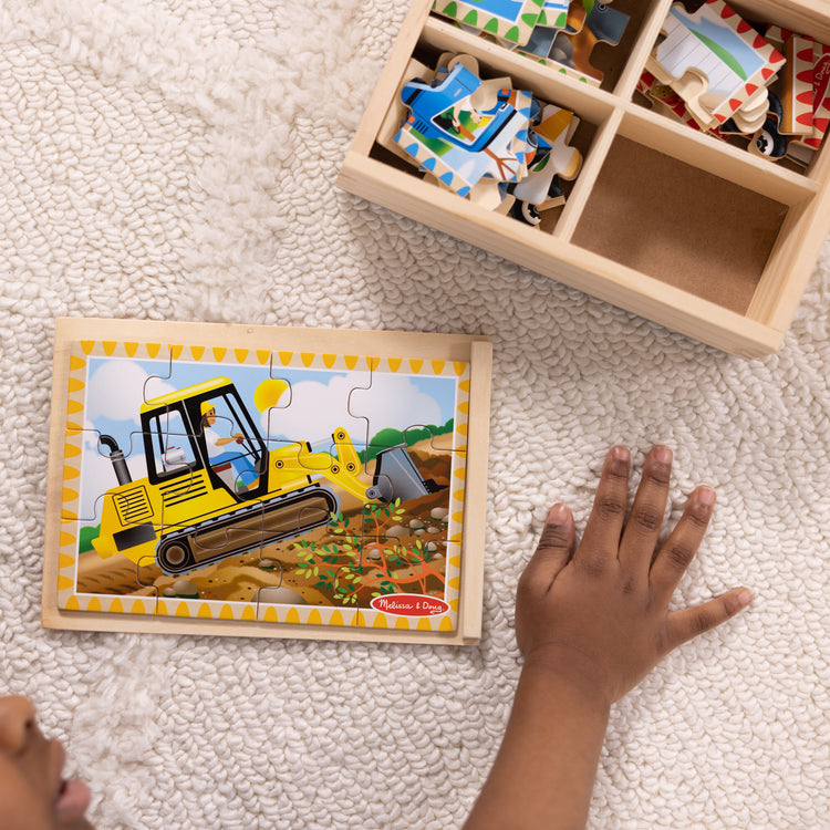 A kid playing with The Melissa & Doug Construction Vehicles 4-in-1 Wooden Jigsaw Puzzles in a Box (48 pcs)