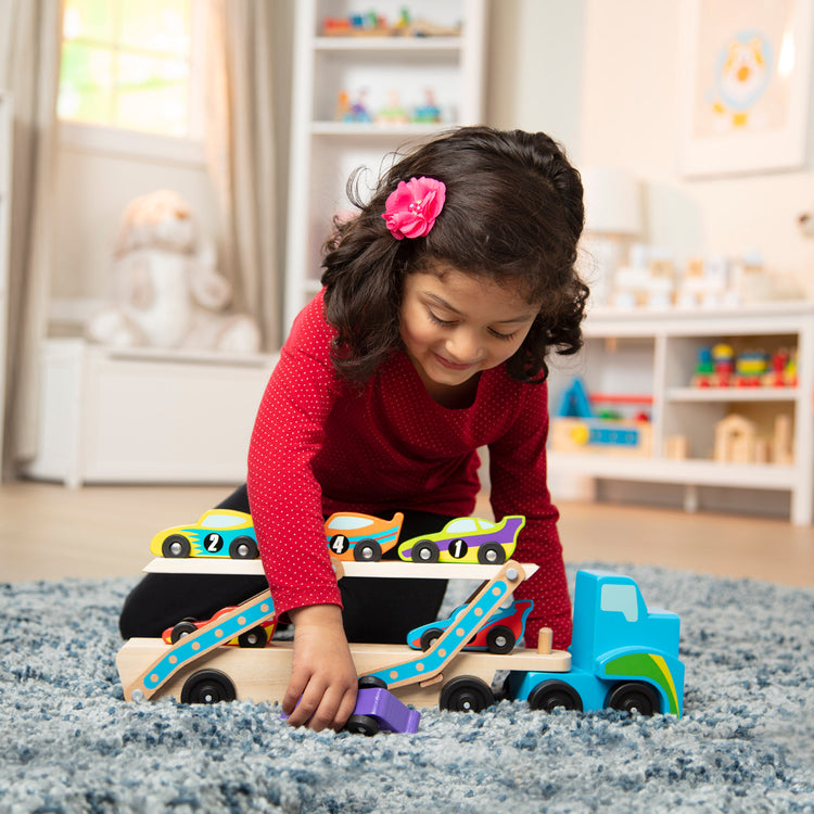 A kid playing with The Melissa & Doug Mega Race-Car Carrier - Wooden Tractor and Trailer With 6 Unique Race Cars