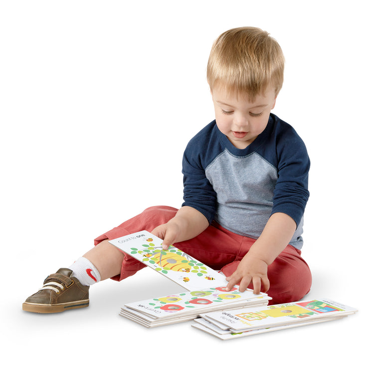 A child on white background with The Melissa & Doug Poke-A-Dot Jumbo Number Learning Cards - 13 Double-Sided Numbers, Shapes, and Colors Cards with Buttons to Pop