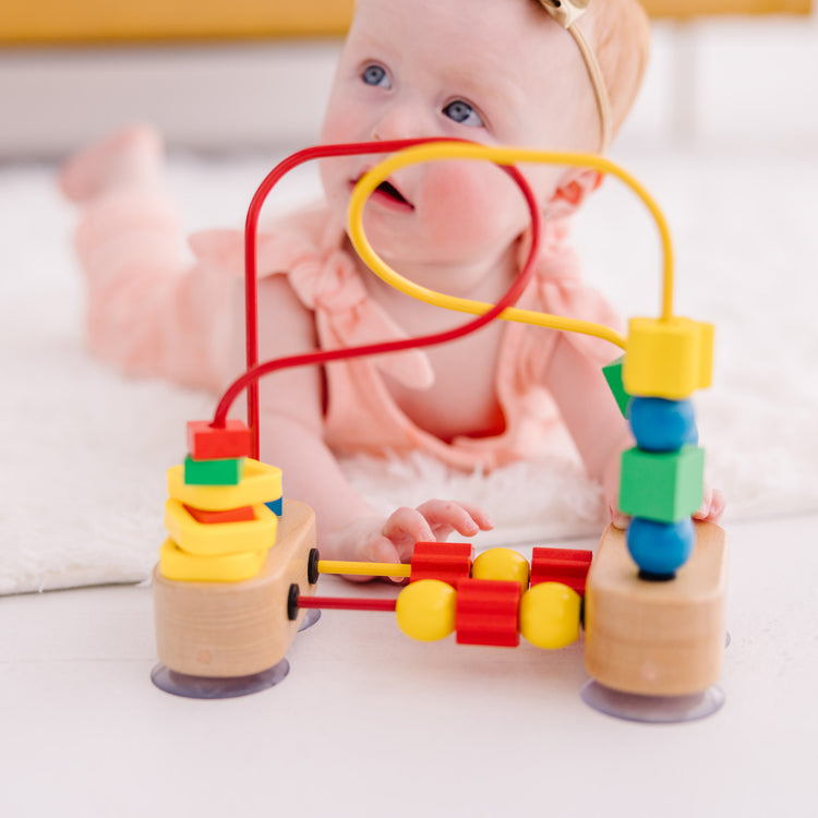 A kid playing with The Melissa & Doug First Bead Maze - Wooden Educational Toy for Floor, High Chair, or Table