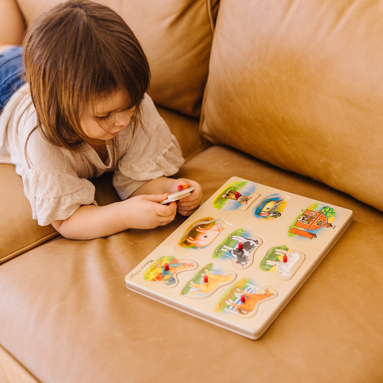 A kid playing with The Melissa & Doug Farm Sound Puzzle - Wooden Peg Puzzle With Sound Effects (8 pcs)