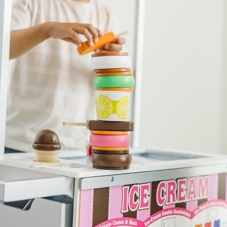 A kid playing with The Melissa & Doug Wooden Snacks and Sweets Food Cart - 40+ Play Food pcs, Reversible Awning