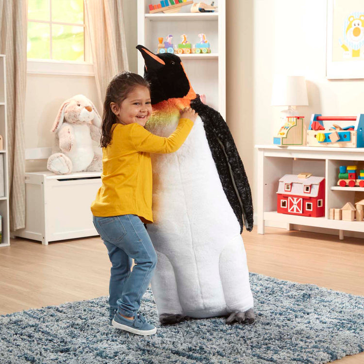 A kid playing with The Melissa & Doug Giant Lifelike Plush Emperor Penguin Standing Stuffed Animal (3.4 Feet Tall)