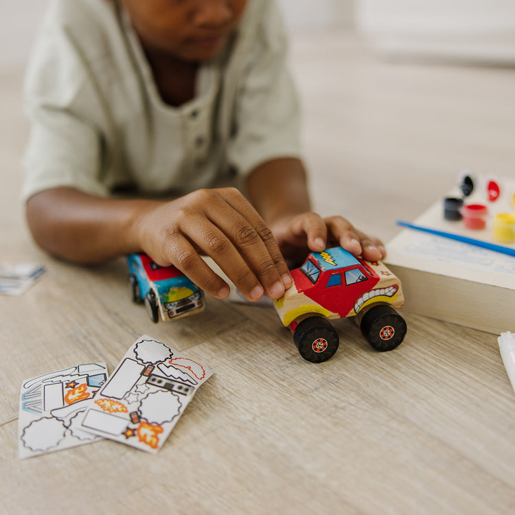 A kid playing with The Melissa & Doug Decorate-Your-Own Wooden Craft Kits Set - Race Car and Monster Truck