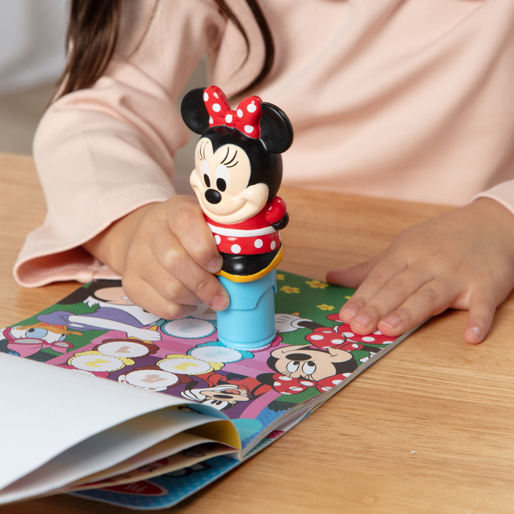 A kid playing with The Melissa & Doug Sticker WOW!™ 24-Page Activity Pad and Sticker Stamper, 300 Stickers, Arts and Crafts Fidget Toy Collectible Character – Disney Minnie Mouse