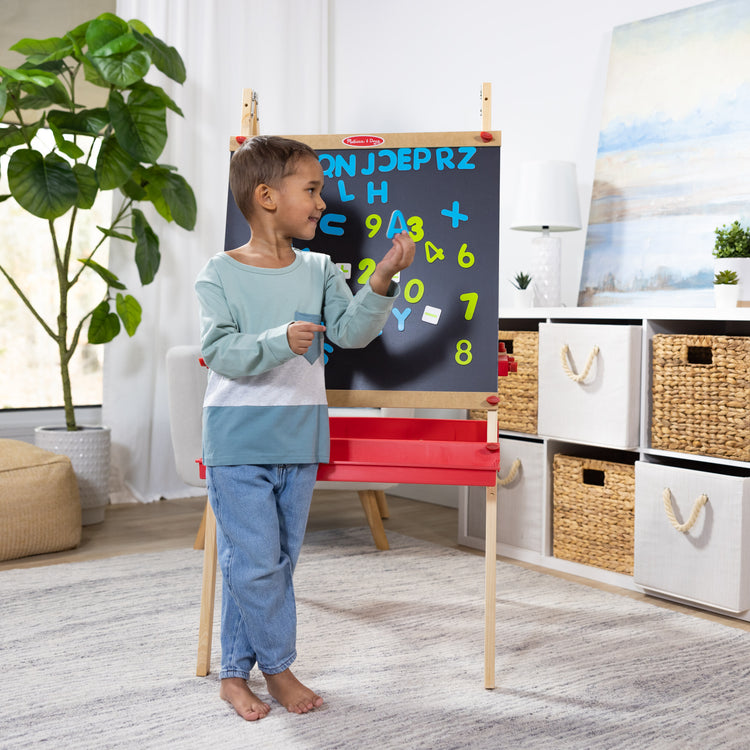 A kid playing with The Melissa & Doug Deluxe Magnetic Standing Art Easel With Chalkboard, Dry-Erase Board, and 39 Letter and Number Magnets