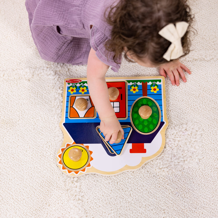 A kid playing with The Melissa & Doug First Shapes Jumbo Peg Wooden Puzzle