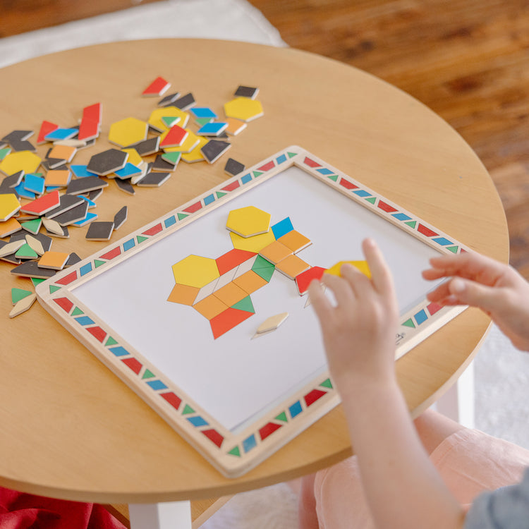 A kid playing with The Melissa & Doug Deluxe Wooden Magnetic Pattern Blocks Set - Educational Toy With 120 Magnets and Carrying Case