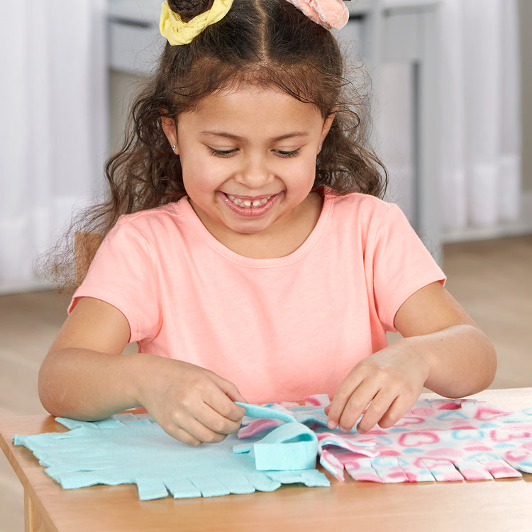 A kid playing with The Melissa & Doug Created by Me! Heart Fleece Blanket No-Sew Craft Kit (40 squares, 3.5 feet x 5 feet)