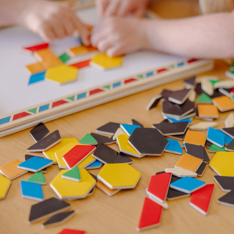 A kid playing with The Melissa & Doug Deluxe Wooden Magnetic Pattern Blocks Set - Educational Toy With 120 Magnets and Carrying Case