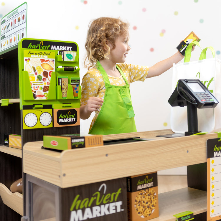 A kid playing with The Melissa & Doug Harvest Market Grocery Store and Companion Collection Accessories
