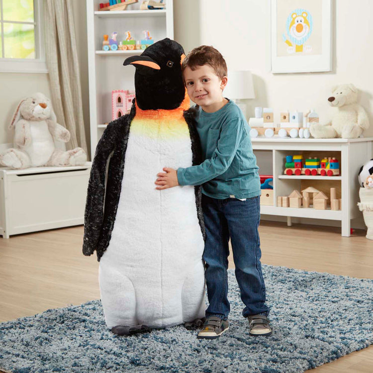 A kid playing with The Melissa & Doug Giant Lifelike Plush Emperor Penguin Standing Stuffed Animal (3.4 Feet Tall)