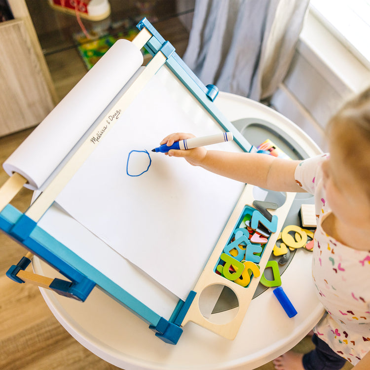 A kid playing with The Melissa & Doug Tabletop Easel Paper Roll (12 inches x 75 feet), 3-Pack