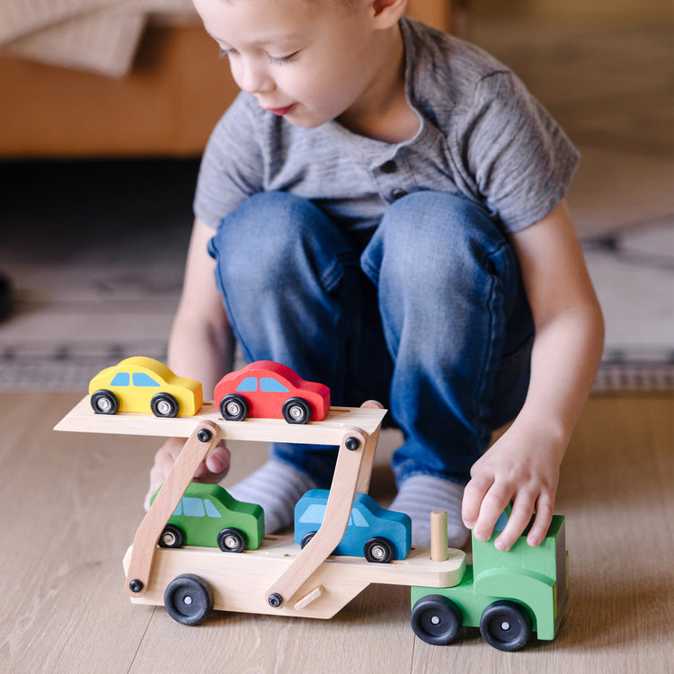 A kid playing with The Melissa & Doug Car Carrier Truck and Cars Wooden Toy Set With 1 Truck and 4 Cars