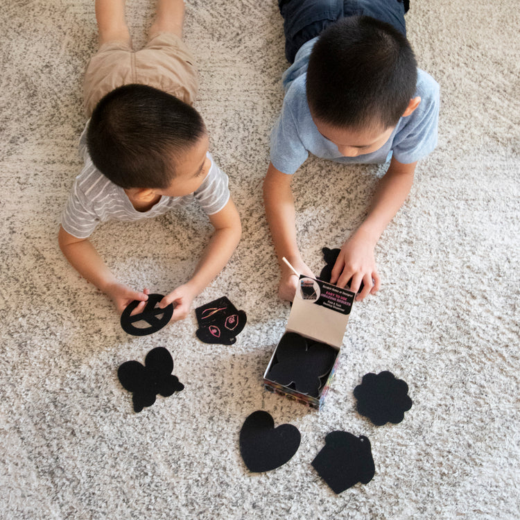 A kid playing with The Melissa & Doug Scratch Art® Box of 125 Friendship-Themed Shaped Notes in Desktop Dispenser (Approx. 3.5” x 3.5” Each Note)