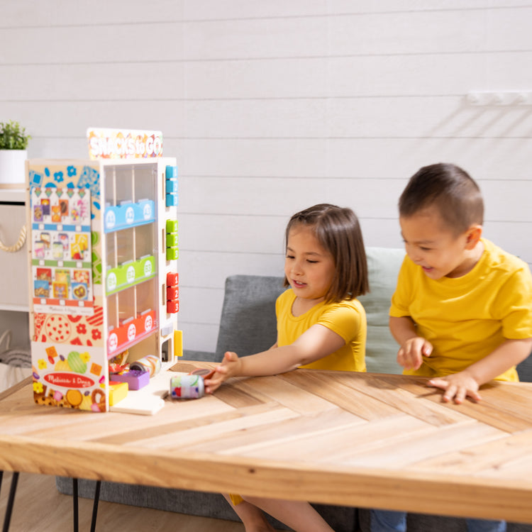 A kid playing with The Melissa & Doug Sort, Stock, Select Wooden Vending Machine Play Set, Wooden Toy Play Food For Boys and For Girls 3+