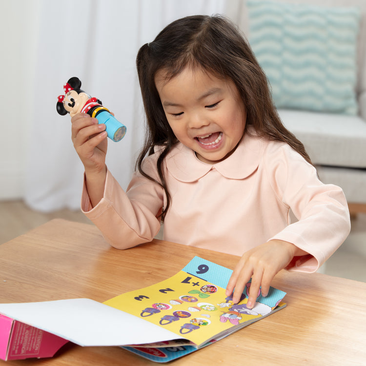 A kid playing with The Melissa & Doug Sticker WOW!™ 24-Page Activity Pad and Sticker Stamper, 300 Stickers, Arts and Crafts Fidget Toy Collectible Character – Disney Minnie Mouse