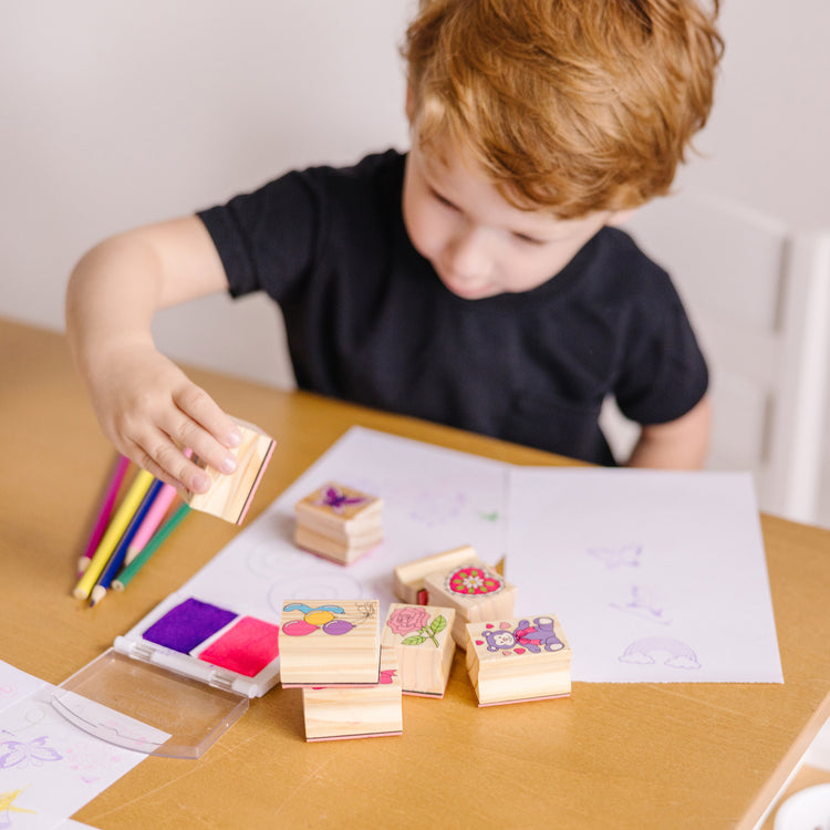 A kid playing with The Melissa & Doug Wooden Stamp Set: Friendship - 9 Stamps, 5 Colored Pencils, and 2-Color Stamp Pad