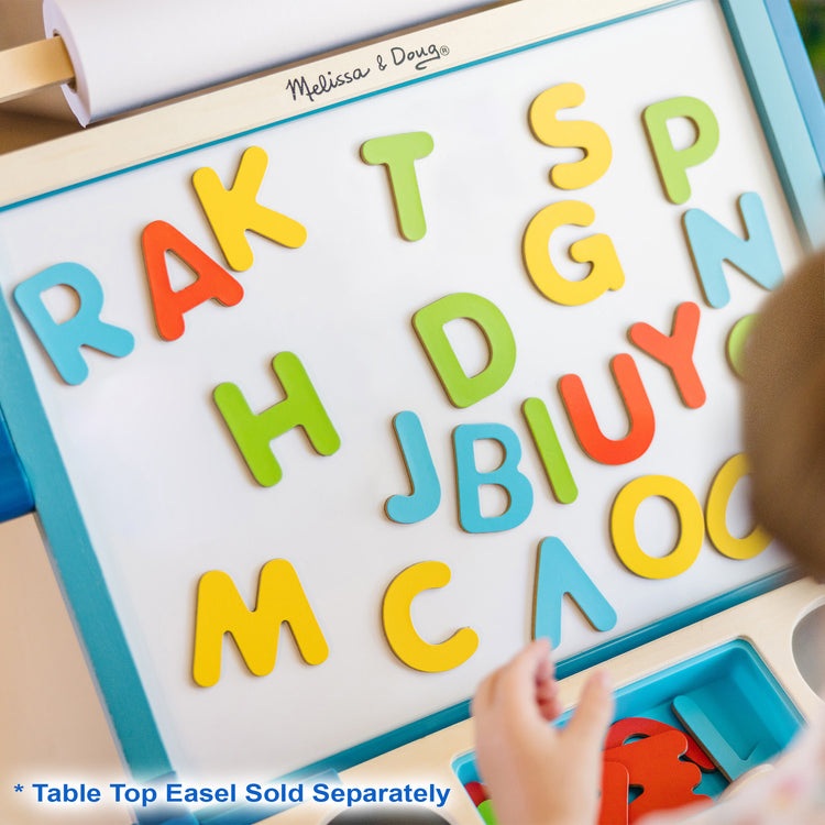 A kid playing with The Melissa & Doug 52 Wooden Alphabet Magnets in a Box - Uppercase and Lowercase Letters