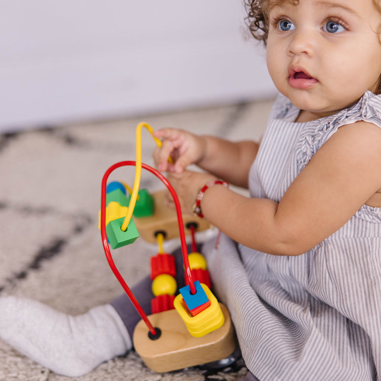 A kid playing with The Melissa & Doug First Bead Maze - Wooden Educational Toy for Floor, High Chair, or Table