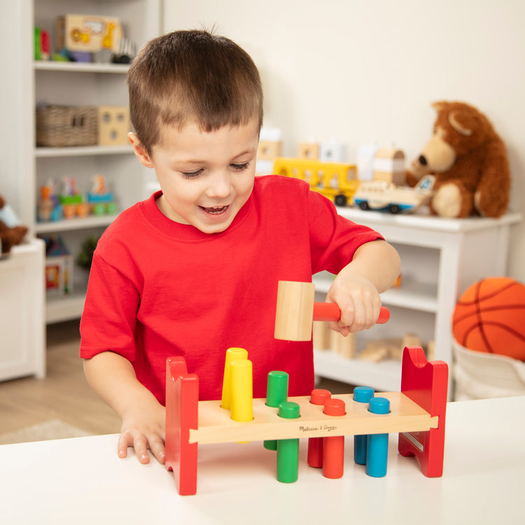 A kid playing with The Melissa & Doug Deluxe Wooden Pound-A-Peg Toy With Hammer