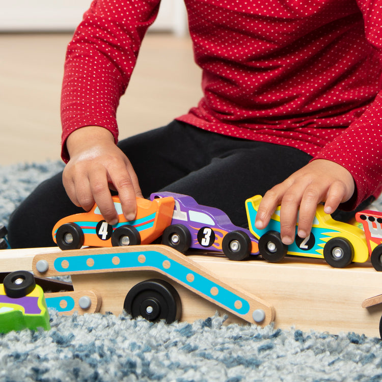 A kid playing with The Melissa & Doug Mega Race-Car Carrier - Wooden Tractor and Trailer With 6 Unique Race Cars